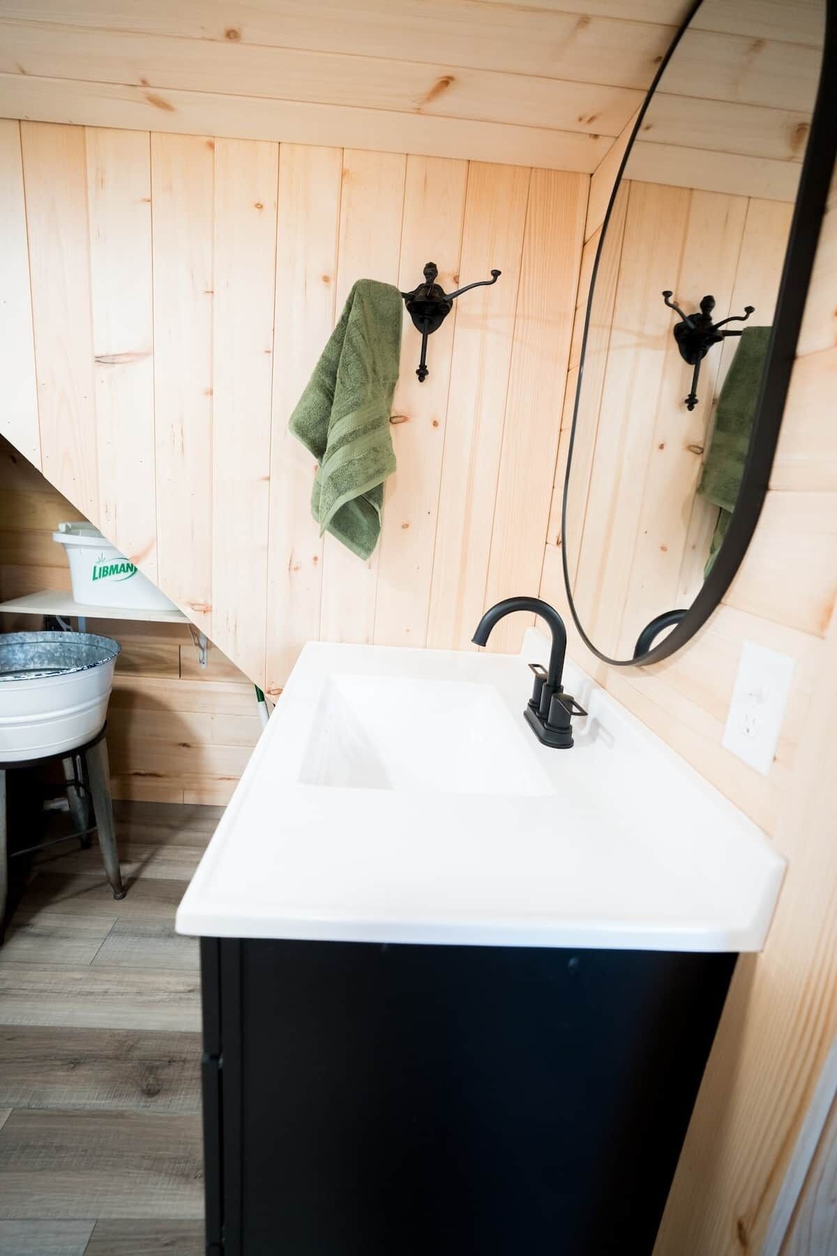 A bathroom with a white sink, black cabinet, wooden walls, and a mirror.