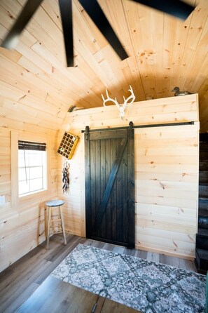 A wooden interior with a sliding barn door, a ladder, a window, and a decorative antler.