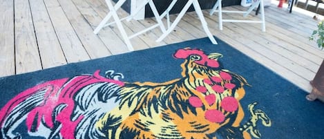 A wooden deck with a colorful rug featuring a tiger design, a white metal chair, and a door.