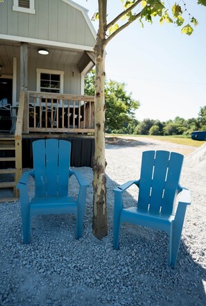 Two blue Adirondack chairs outside a building with a wooden deck and a gravel ground.