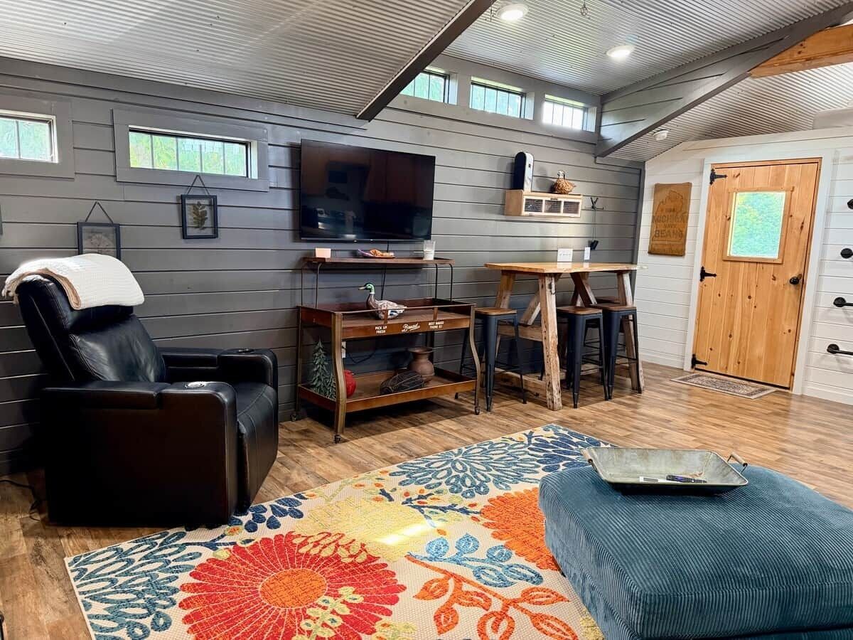 Una habitación con sillón de masaje, televisor, mesa de madera y alfombra estampada.