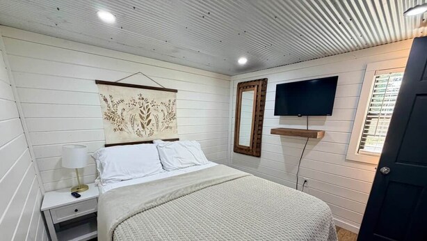 A bedroom with a bed, a nightstand, a wall-mounted TV, and a door.