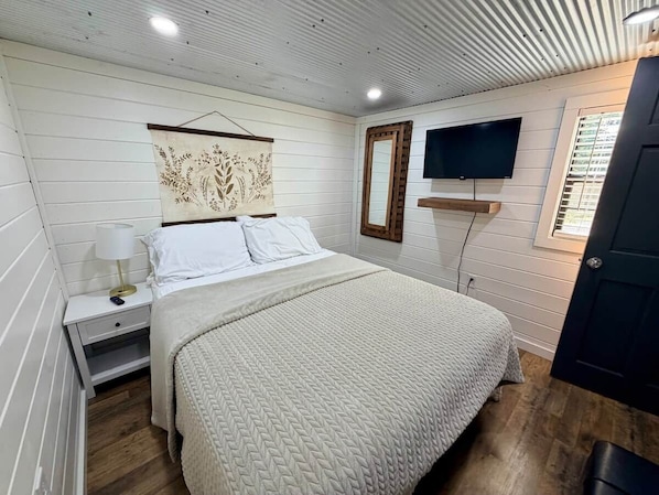 A bedroom with a bed, a nightstand, a wall-mounted TV, and a door.