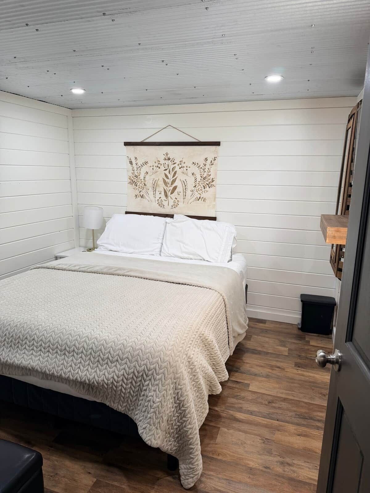 Ein Schlafzimmer mit einem Bett, einer Wandweberei, einer Nachttischlampe und Holzboden.
