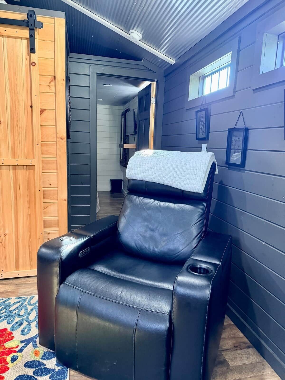 A massage chair in a room with dark walls, a wooden door, and a small window.