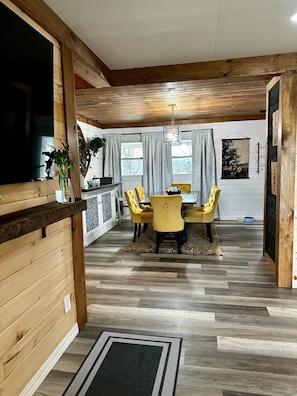 A dining area with a wooden ceiling, a dining table with yellow chairs, and a kitchen area with a plant and a window. - Hot Tub + Pet Friendly / Perfect for travel ball (Paducah)