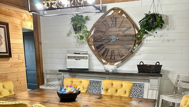 A dining area with a wooden table, yellow chairs, a large wall clock, and a hanging plant. - Hot Tub + Pet Friendly / Perfect for travel ball (Paducah)