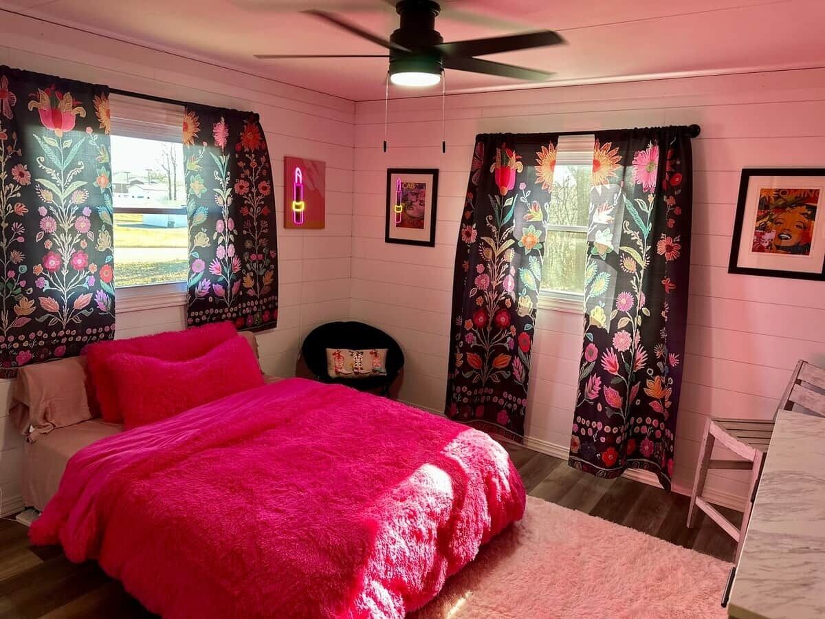Una camera da letto con un letto, una sedia, una ventola a soffitto e tende a motivi floreali.