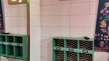 Une salle de bain avec un miroir, des œuvres d’art à base de néons et des étagères de rangement.