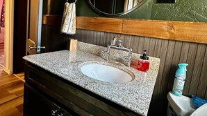 A bathroom with a granite countertop sink, a wooden vanity, a round mirror, and a toilet. - Hot Tub + Pet Friendly / Perfect for travel ball (Paducah)