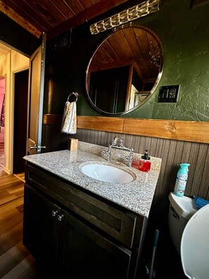 A bathroom with a granite countertop sink, a wooden vanity, a round mirror, and a toilet. - Hot Tub + Pet Friendly / Perfect for travel ball (Paducah)