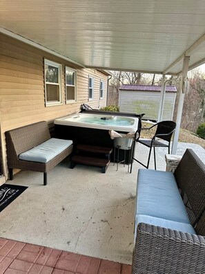 A covered patio area with a hot tub, wicker furniture, and a small shed in the background. - Hot Tub + Pet Friendly / Perfect for travel ball (Paducah)