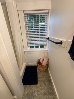 Ein kleines Badezimmer mit Fenster, Handtuchhalter, Korb und schwarzer Matte.