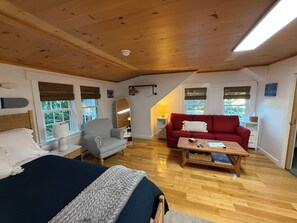 Una habitació acollidora amb un llit, un sofà vermell, un butac armchair a ratlles, una taula de centre de fusta i un mirall gran.
