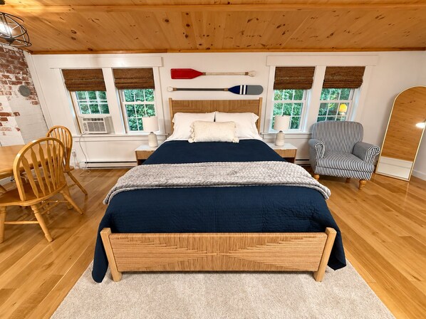 Un dormitorio con cama de madera, una silla, un sillón a rayas y una ventana con vista a árboles.