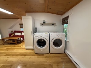 Ein Waschraum mit zwei weißen Waschmaschinen, Holzboden, einer roten Couch und einer Holzzahl.