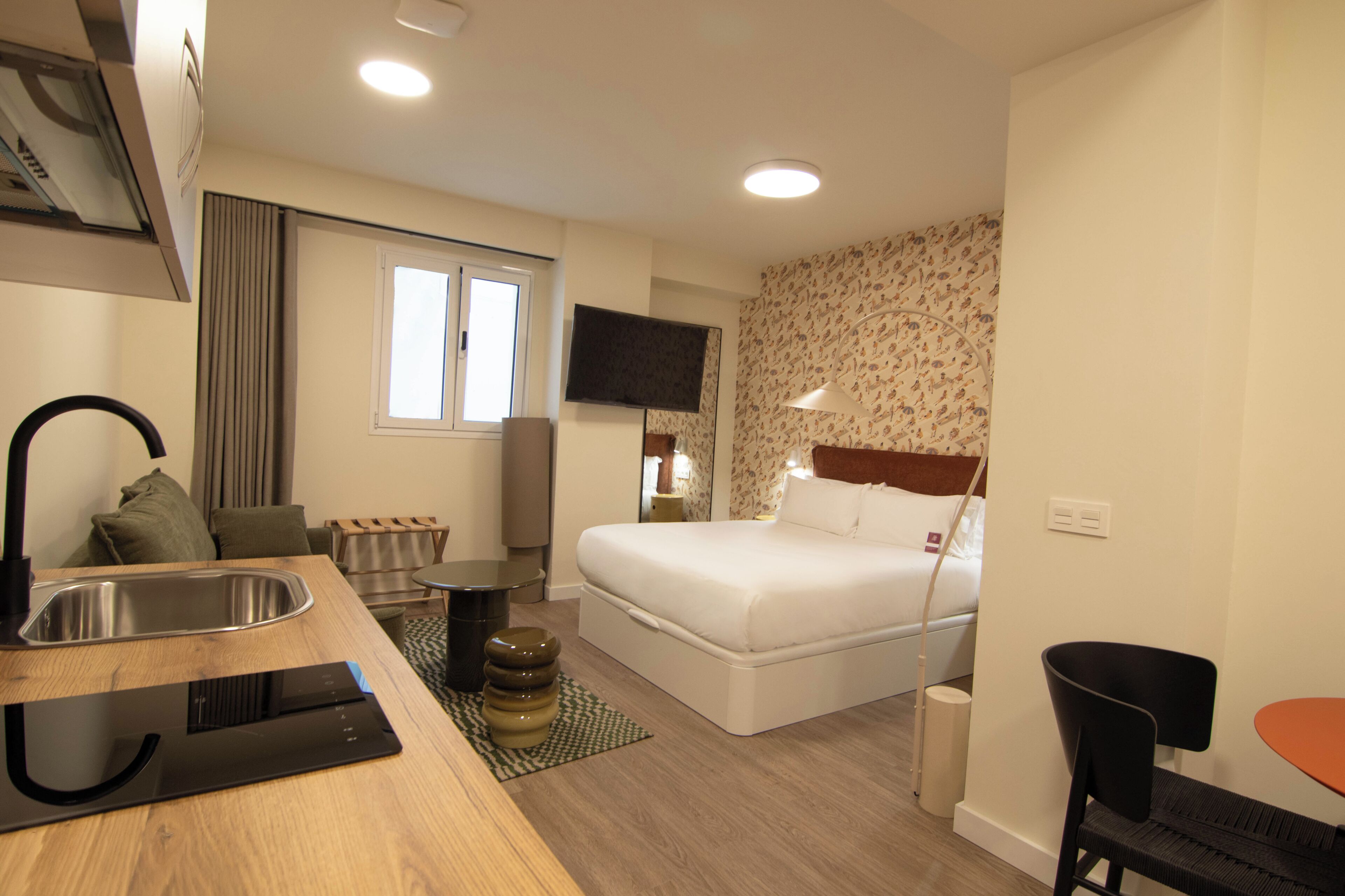 Ein Hotelzimmer mit Bett, Schreibtisch mit Waschbecken, Fernseher und einer Wand mit Muster.