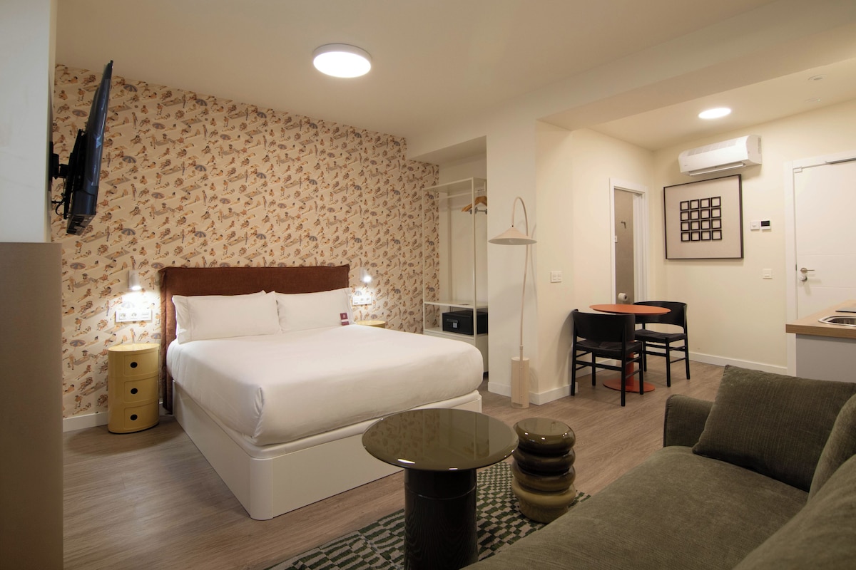 A hotel room with a bed, a desk, a chair, a sofa, and a TV.