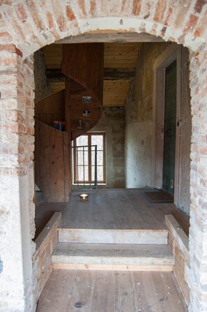 A rustic wooden interior with a brick archway, a wooden staircase, and a large window. - Apartment 'Le Fagotier' with Shared Garden, Balcony and Wi-Fi (Jons)