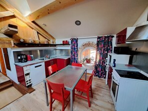 Eine kleine Küche mit Essbereich, Holzbalken und einem Fenster mit Vorhängen.