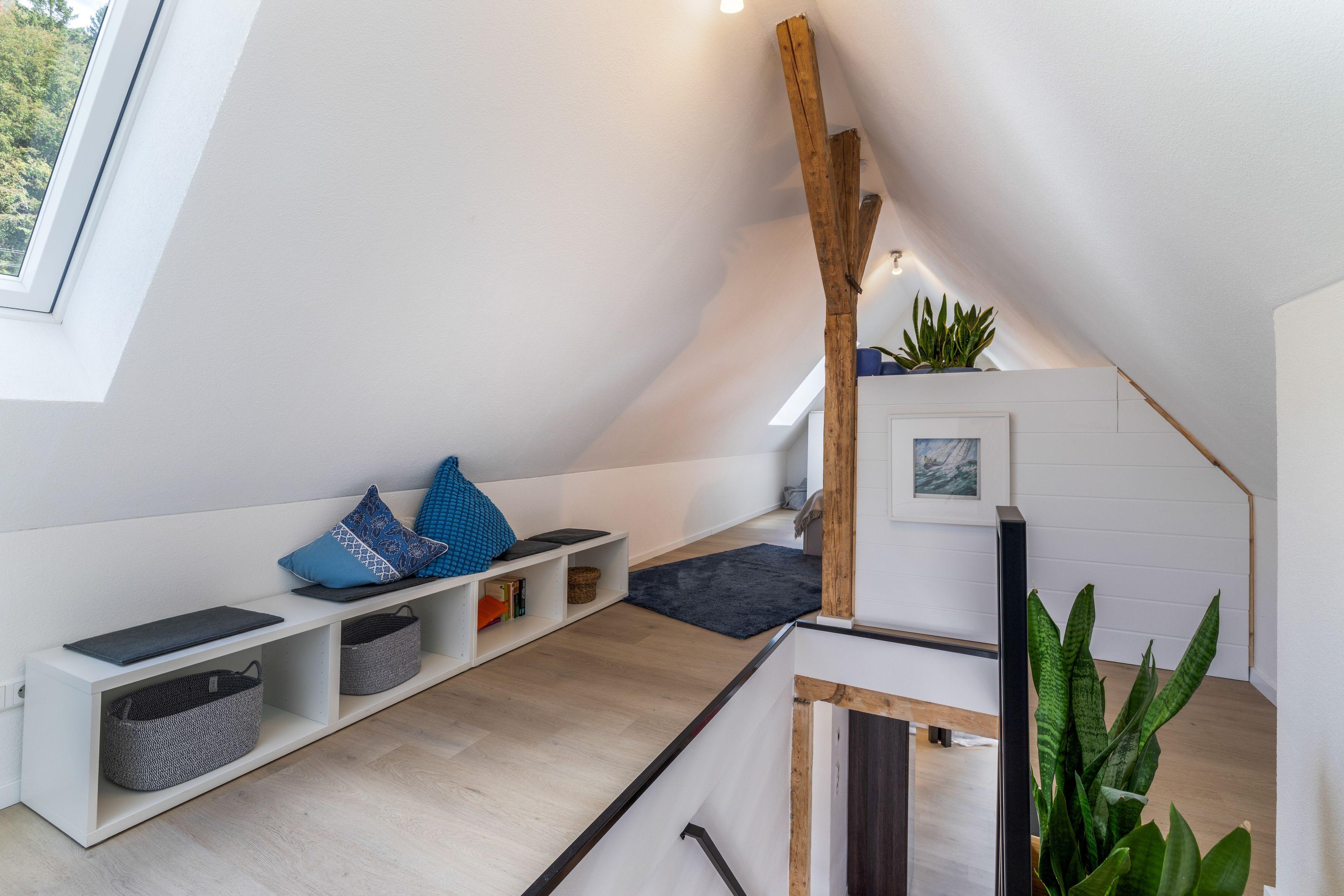 Ein modernes Schlafzimmer im Loft-Stil mit schrägem Dach, eingebauten Regalen, einem dunklen Teppich und einem großen Fenster.