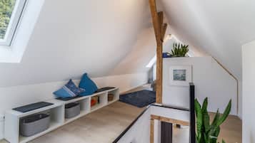 Ein modernes Schlafzimmer im Loft-Stil mit schrägem Dach, eingebauten Regalen, einem dunklen Teppich und einem großen Fenster.
