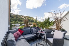Een balkon met een grijze bank, een klein tafeltje en potplanten.