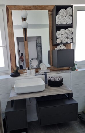 Un bagno moderno con uno specchio grande, un lavandino bianco e asciugamani ordinatamente riposti su mensole.