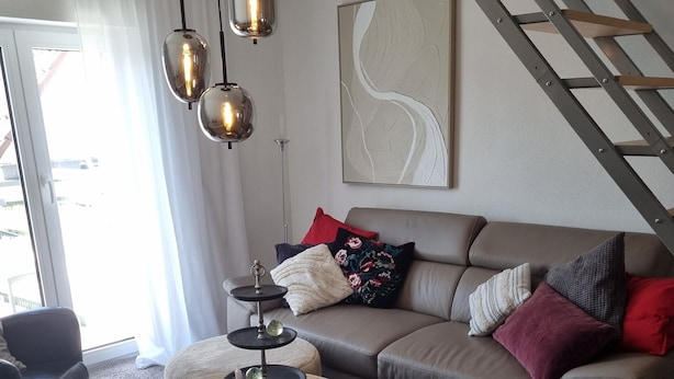 Un saló modern amb un sofà gris, una taula de centre rodona de fusta i una butaca negra.