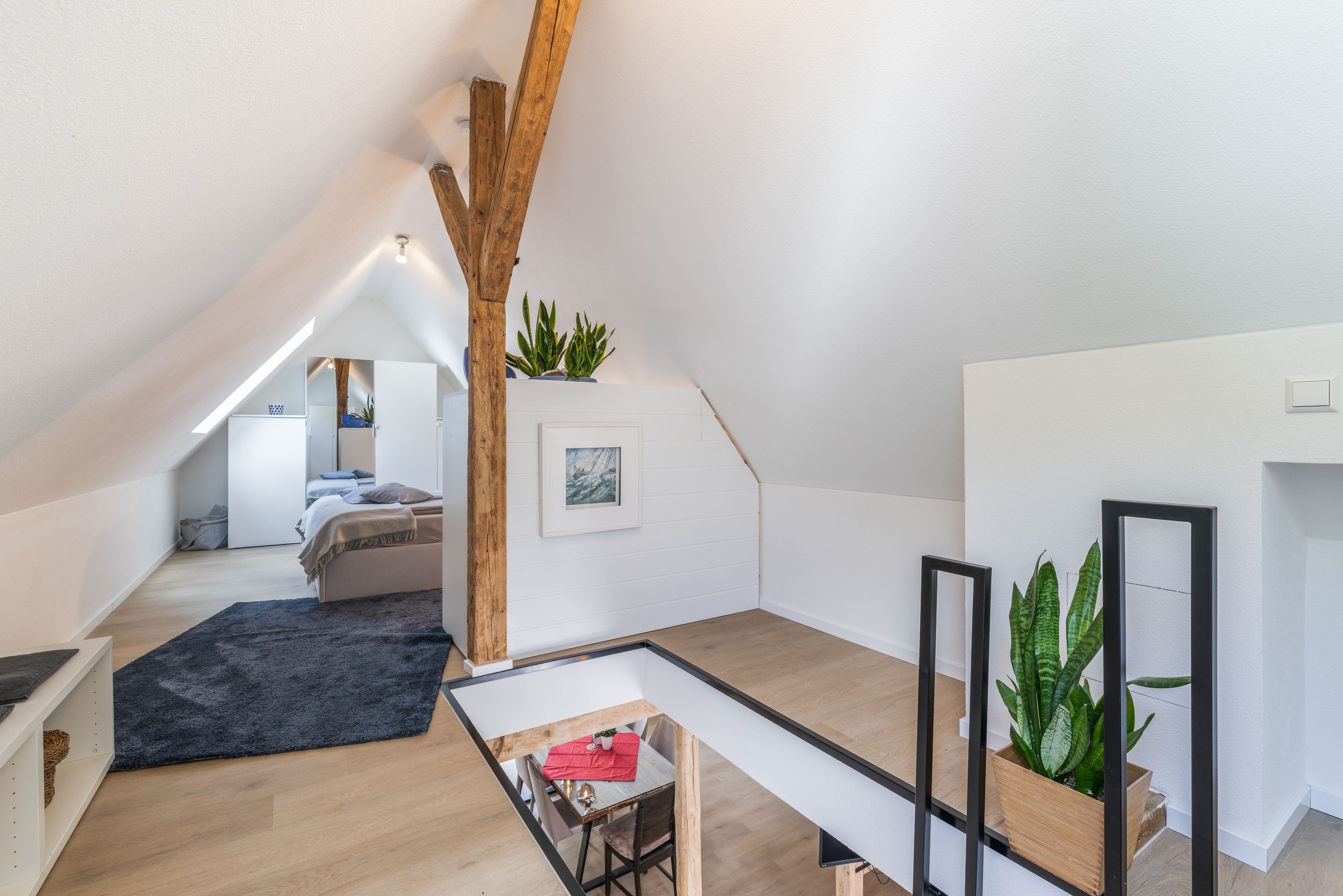 Ein modernes Schlafzimmer im Loft-Stil mit schrägem Dach, einem Bett, einem kleinen Tisch und Topfpflanzen.