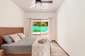 Ein Schlafzimmer mit Bett, Deckenventilator und Blick auf einen Swimmingpool durch eine Glastür.