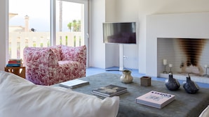 Una sala de estar con sofá, televisor de pantalla plana, chimenea y vistas al exterior.