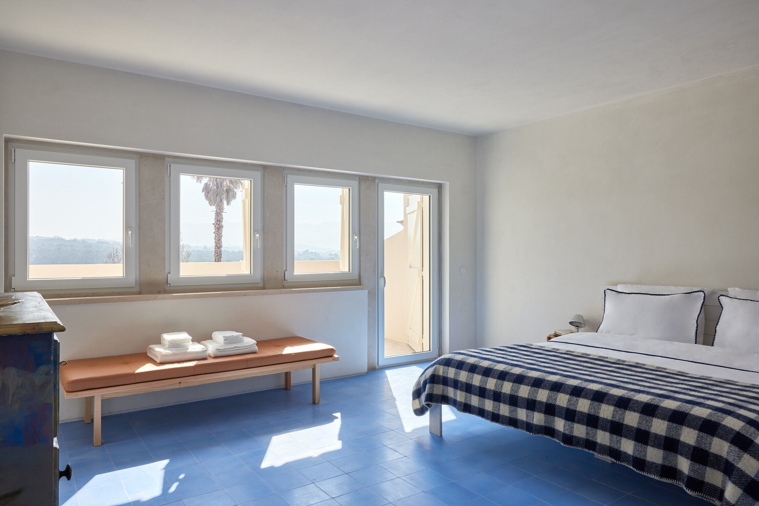 A bedroom with a bed, a bench, and a window with a view.