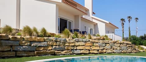 A modern house with a stone retaining wall and a swimming pool.