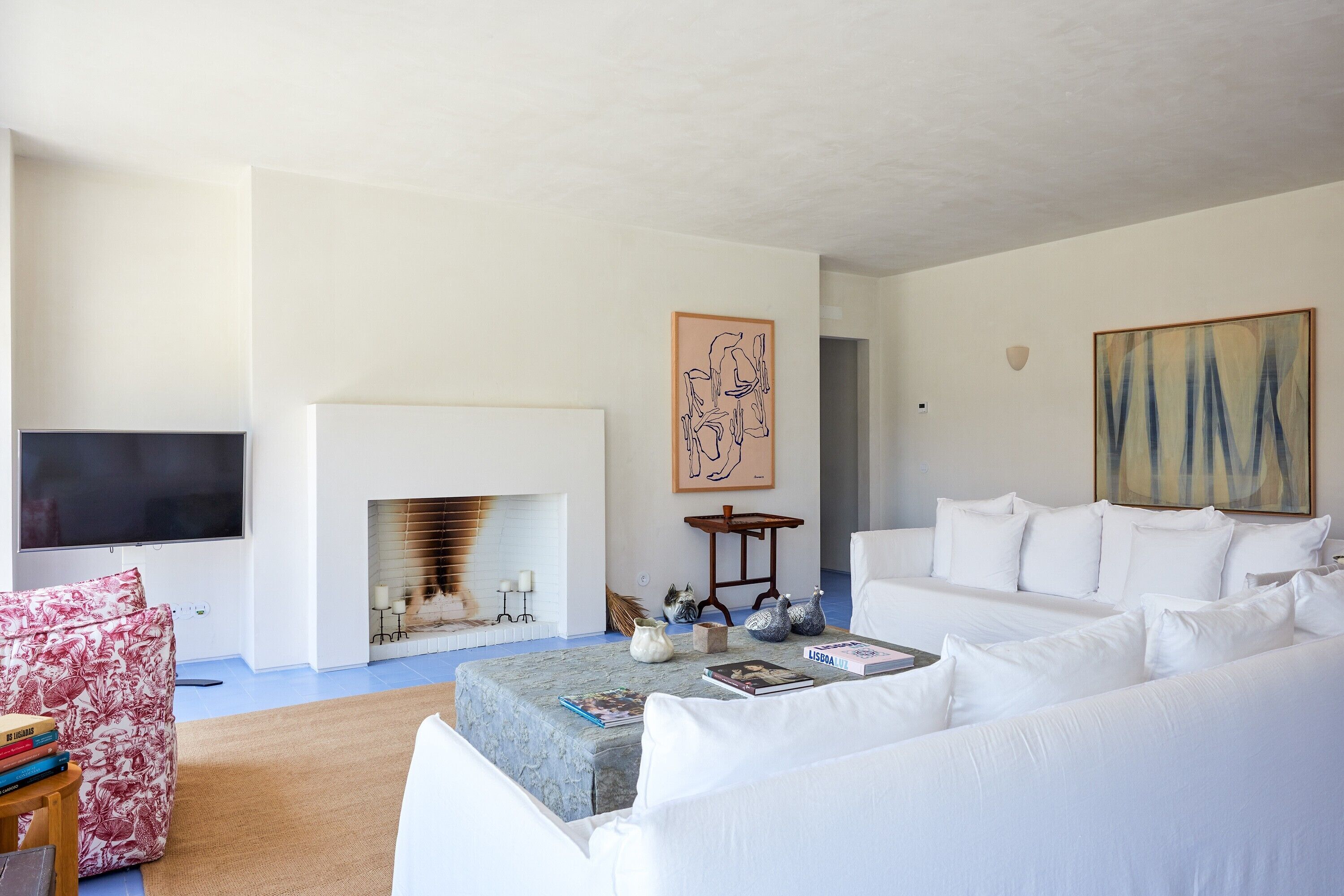 A modern living room with a fireplace, white sofas, a flat-screen TV, and artwork on the walls.