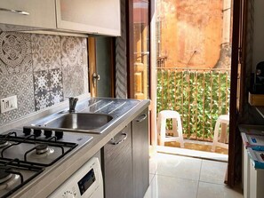 Una cucina con piano cottura a gas, lavello e finestra che dà su un balcone con vista su una recinzione verde.