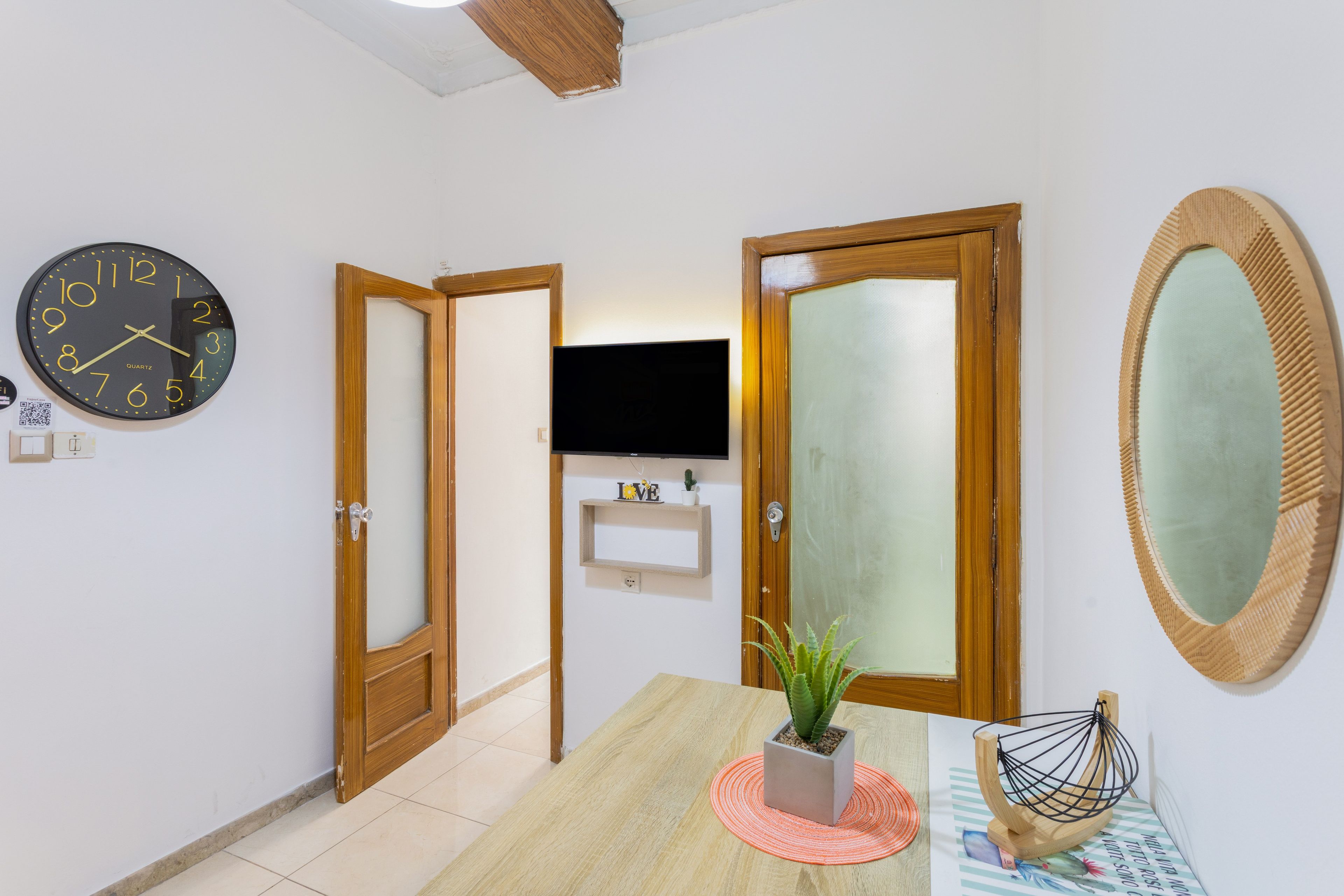 A hallway with a clock, wooden doors, a television, and a mirror.