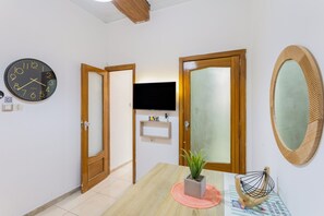 A hallway with a clock, wooden doors, a television, and a mirror.
