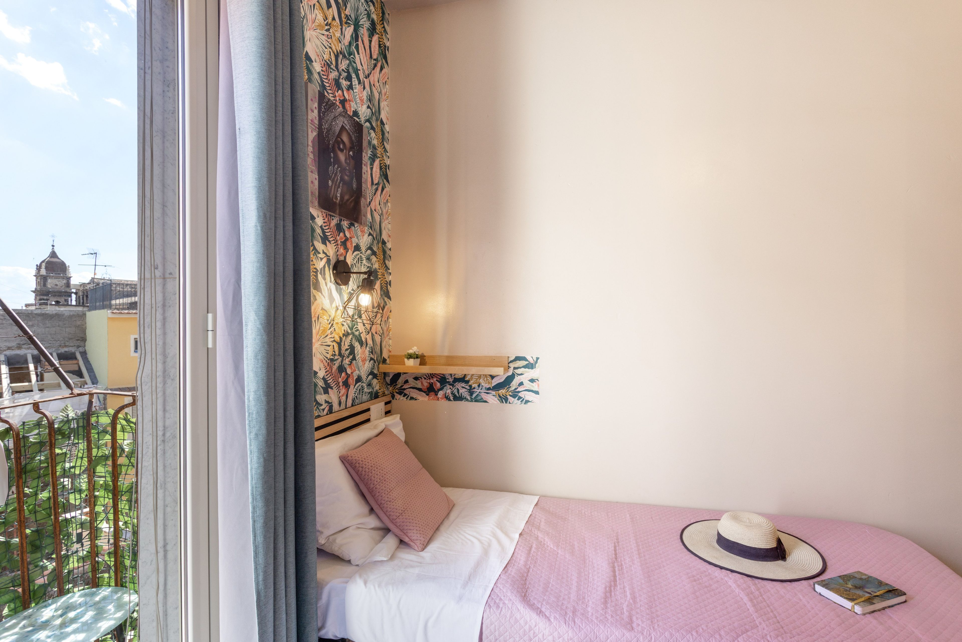 Quarto com cama, janela e vista de um edifício, com um chapéu sobre a cama.