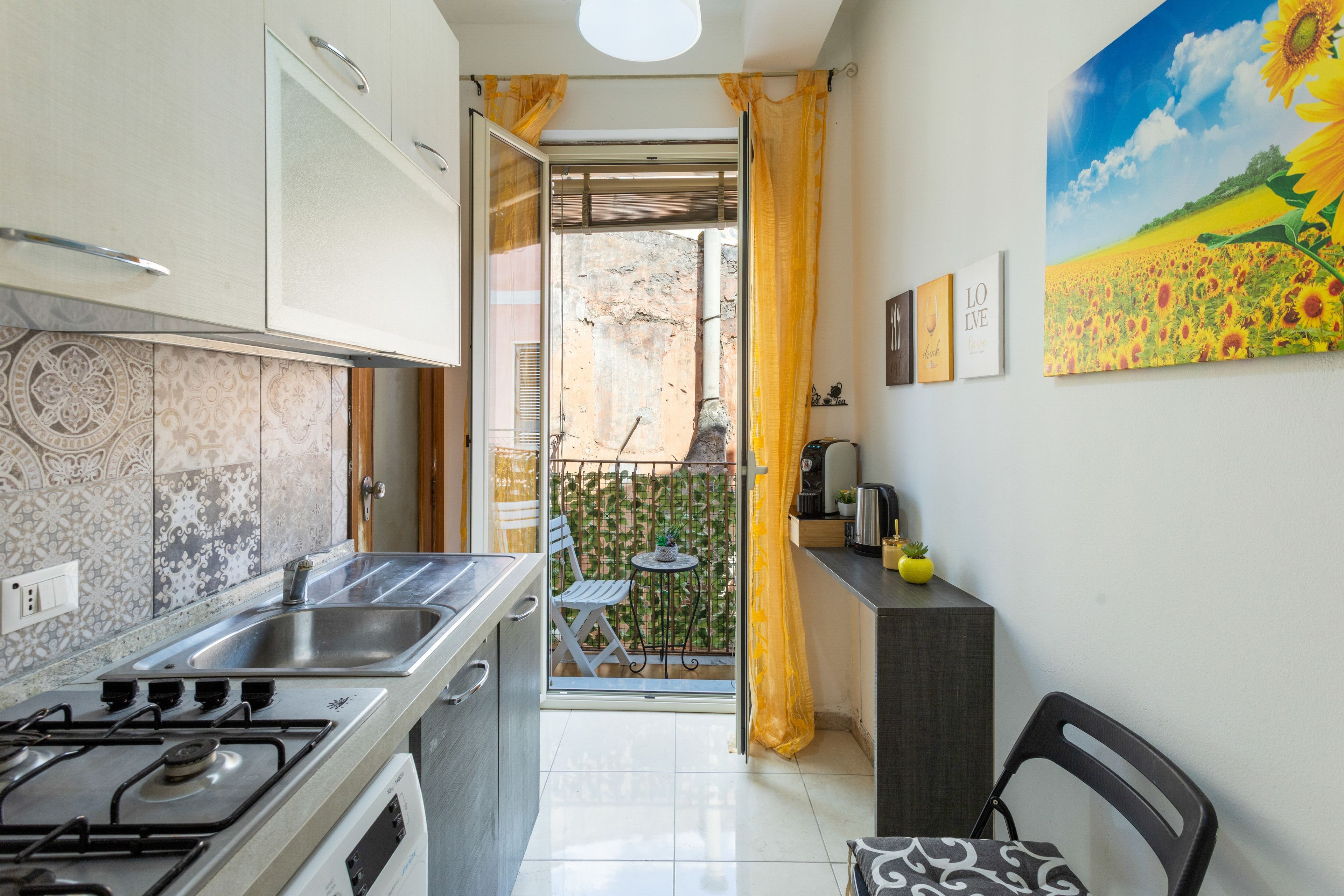 A kitchen with a gas stove, a sink, and a window with a curtain.