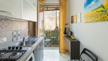 A kitchen with a gas stove, a sink, and a window with a curtain.