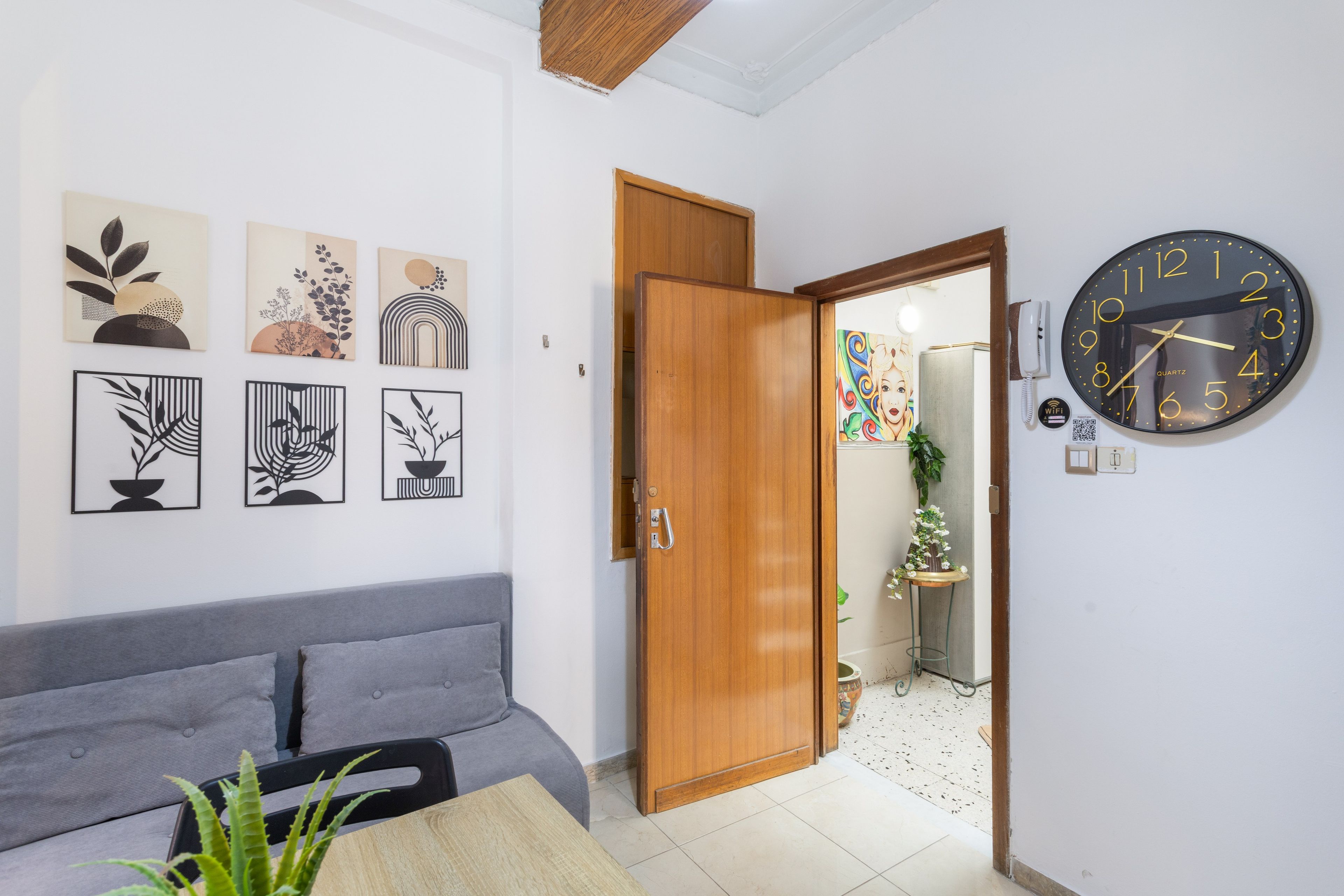 Ein Zimmer mit einem grauen Sofa, einer Holztür und einer Wanduhr.