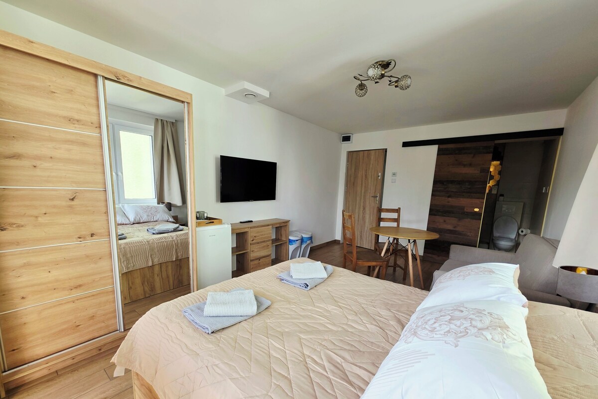 Ett hotellrum med en säng, ett skrivbord, en stol, en tv och ett badrum.