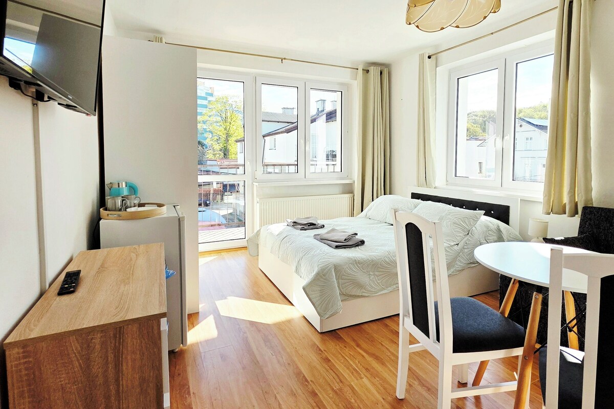 Ett modernt sovrum med en säng, ett skrivbord, en stol, en tv och ett fönster med gardiner.