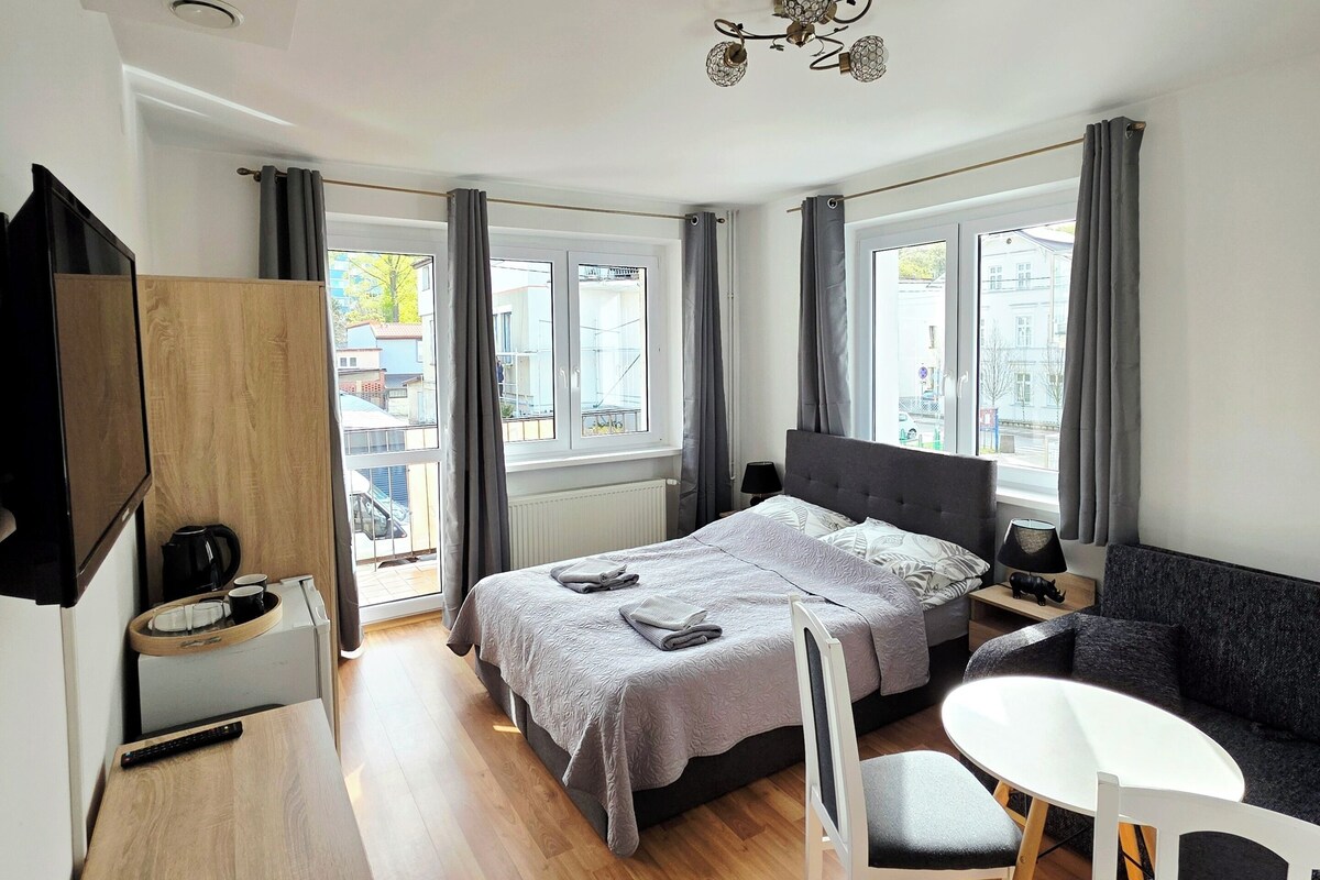 Ett modernt sovrum med en säng, sängbord, en soffa, ett skrivbord och utsikt över omgivningen.