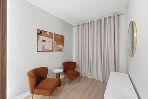 Ein modernes Zimmer mit zwei Sesseln, einem kleinen runden Tisch und einem großen Spiegel an der Wand.