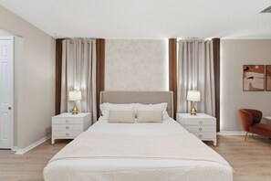 Ein modernes Schlafzimmer mit einem großen Bett, zwei Nachttischen, einem Sessel und einer Wand mit Kunstwerken.