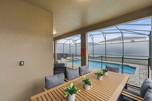 A poolside area with a wooden table, chairs, and potted plants. - 7BR Themed Home | Solara Resort + Game, Cinema (Kissimmee)