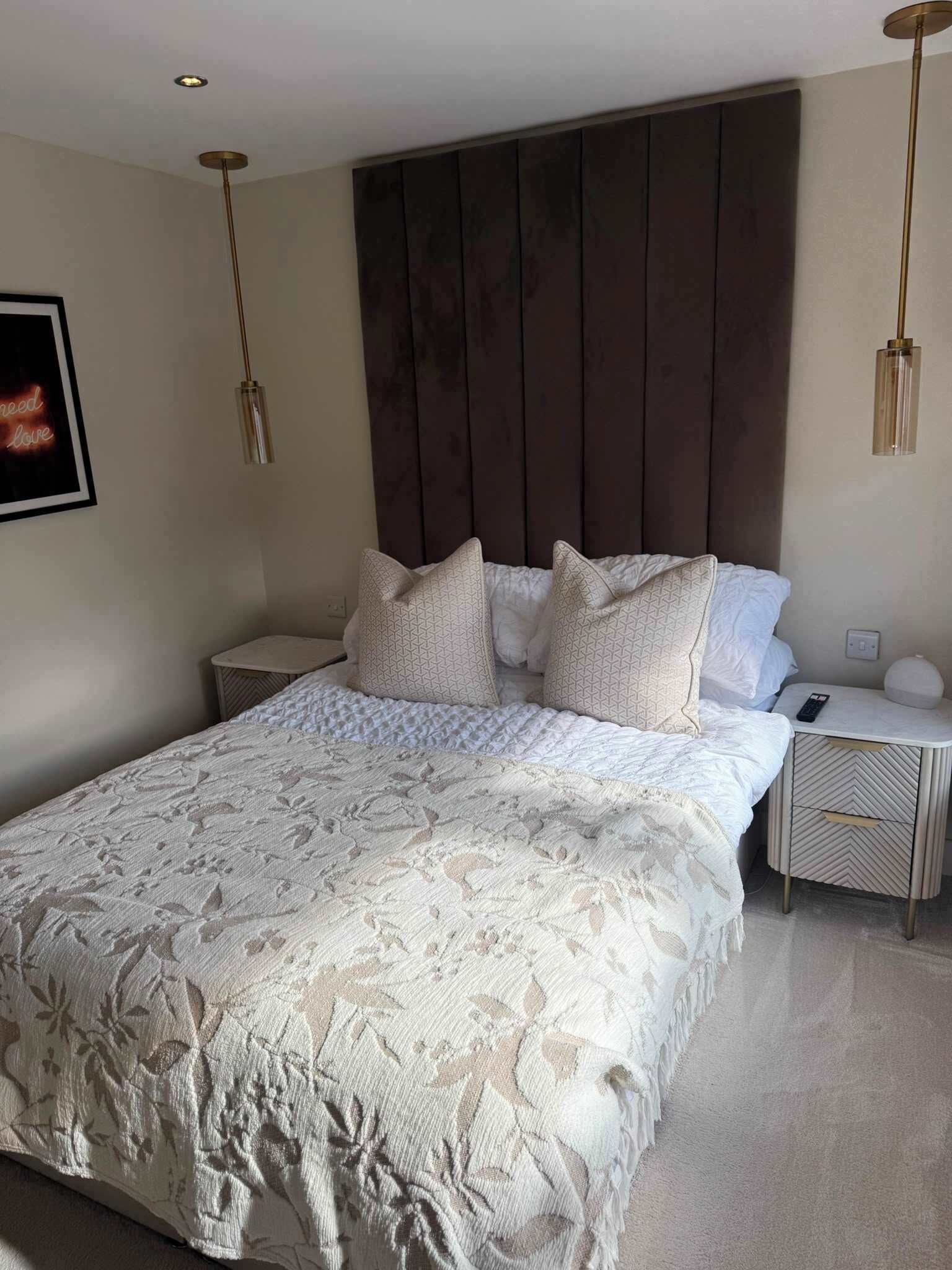 Un dormitorio con una cama grande, dos mesitas de noche, un cabecero y lámparas colgantes.
