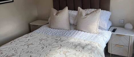 Un dormitorio con una cama grande, dos mesitas de noche, un cabecero y lámparas colgantes.